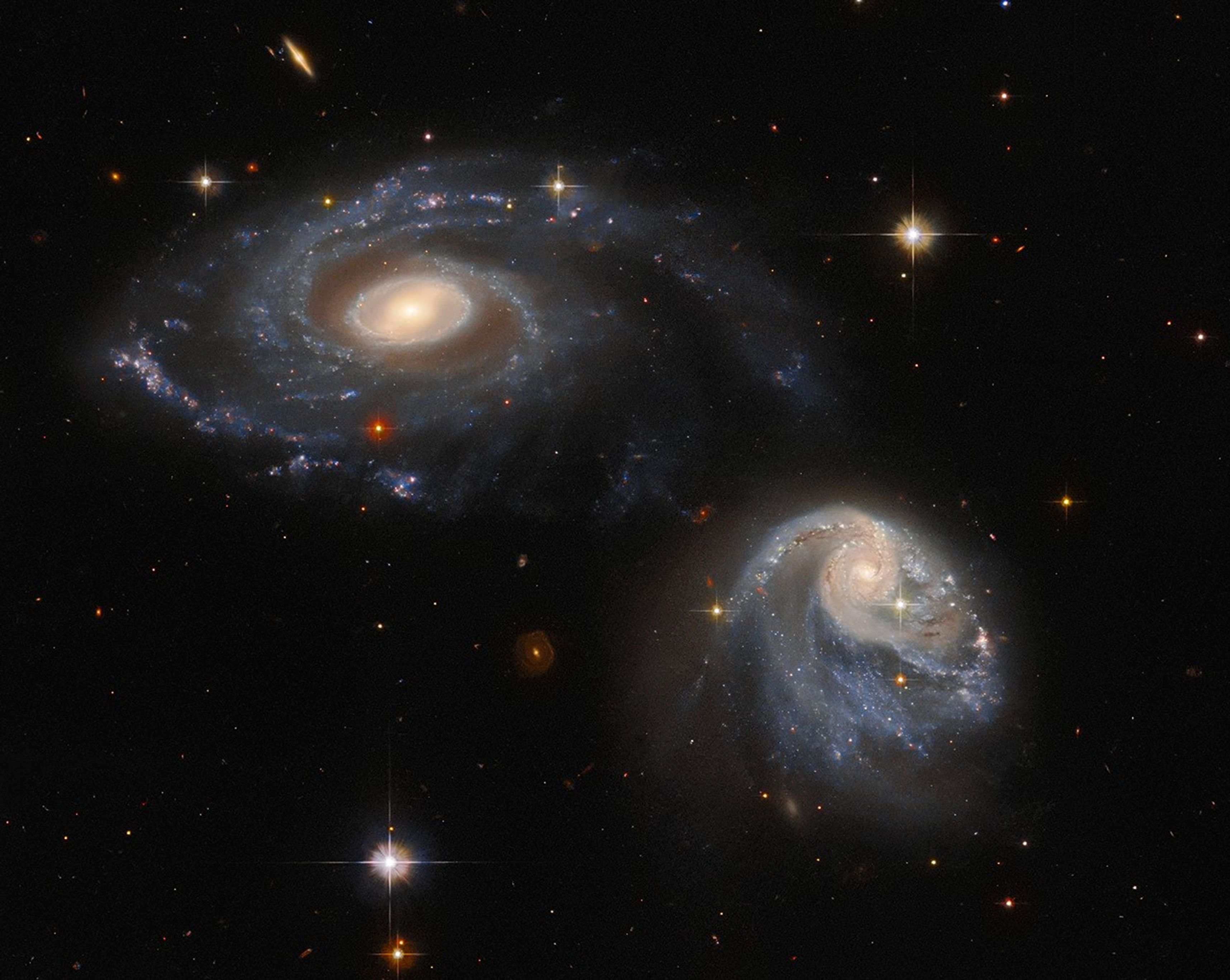 Two spiral galaxies, one at upper-left the other at lower-right, both are nearly face-on providing views of their spiral arms, background stars and galaxies.